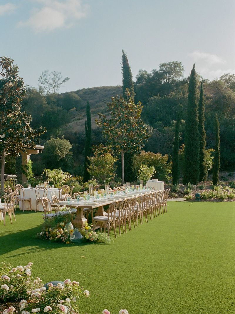 Long reception table set on a lawn beneath cypress and magnolia trees