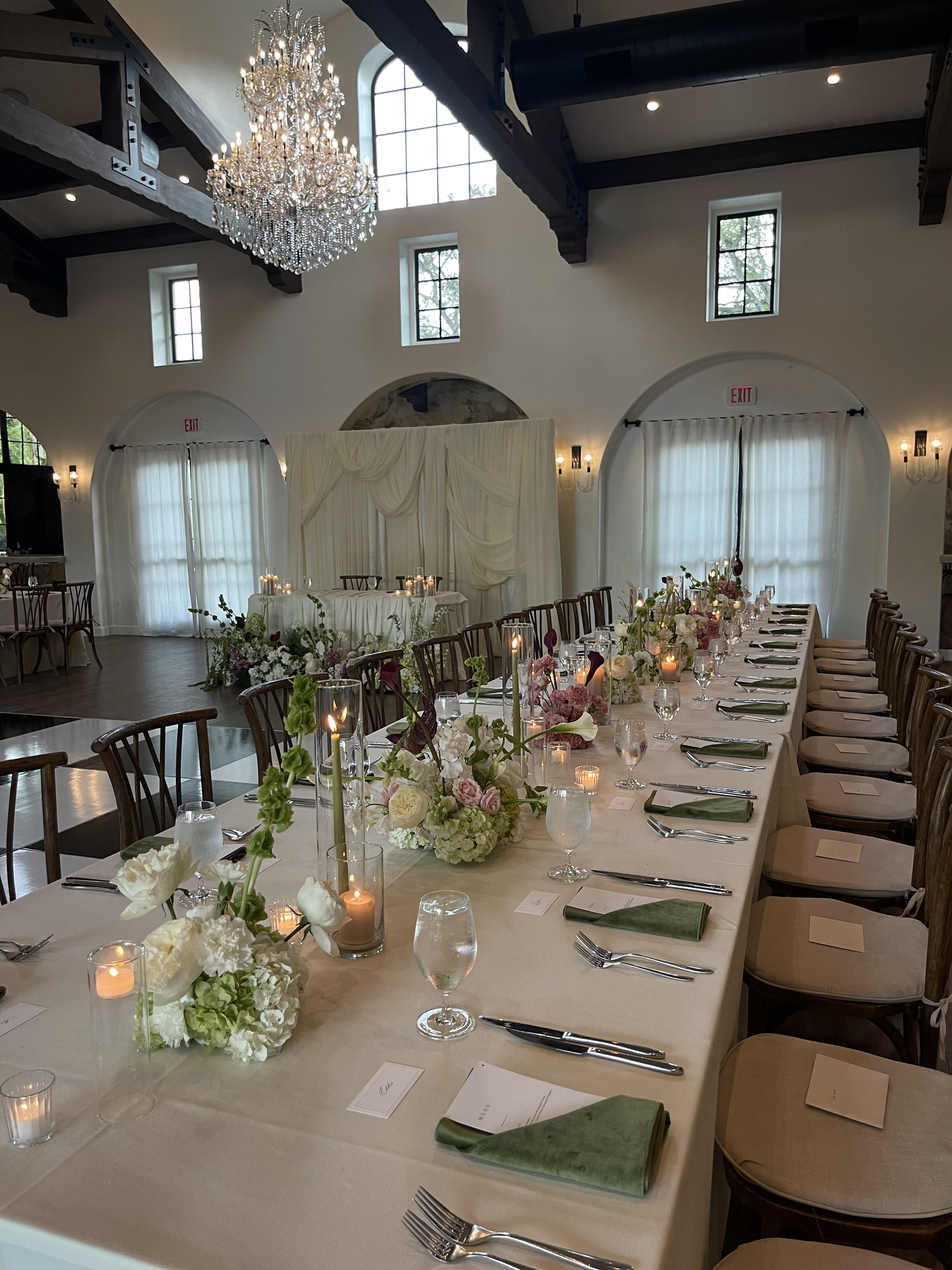 Luxurious reception hall with chandelier, candlelit tablescape and sage green napkins